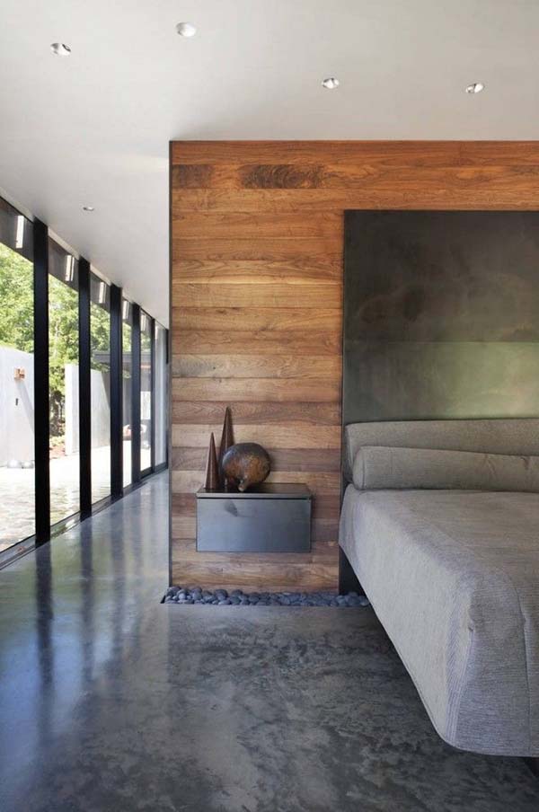 The room feels dark because of the dark gray floor but there is plenty of light from the floor to ceiling glass doors. The wooden feature wall acts to break and divide the open plan living space. A gap exists where the floor meets the feature wall. This is filled with large dark pebbles.