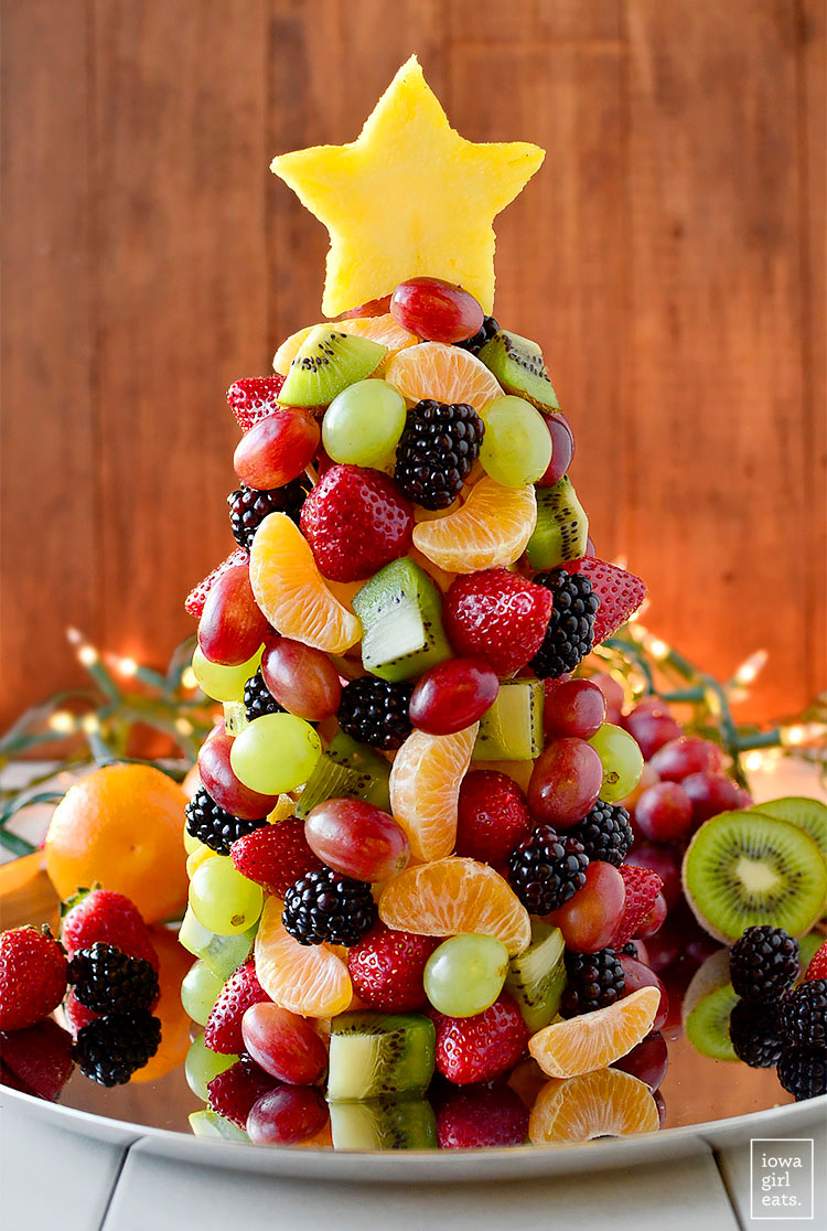 A variety of different cut fruit, grapes, strawberries, kiwi, clementine pieces and pineapple attached to a cone shaped pineapple base with cocktail sticks with a star shaped pineapple piece at the top