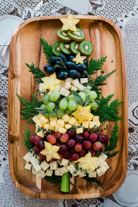 Fruit platter served with different fruit and cheeses arranged in the shape of a Christmas tree on a wooden platter