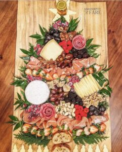 Charcuterie grazing board with food arranged in a the shape of a Christmas tree with cheese, crackers, various nuts and berries, sliced smoked salmon and ham