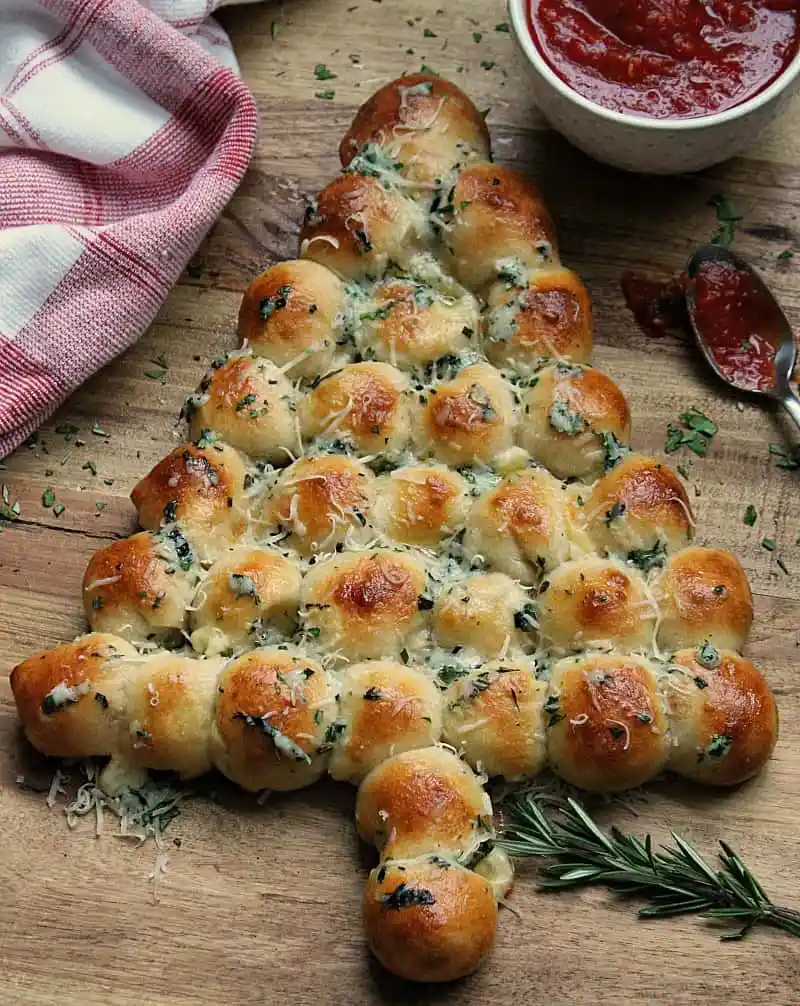 Mozzarella filled round buns arranged in the shape of a Christmas tree with sprinklings of coarsely chopped herbs, rosemary, basil