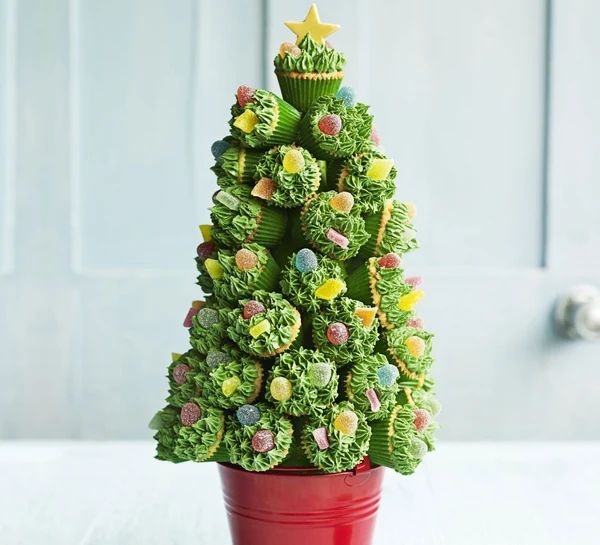 Mini cupcakes attached to a styrofoam cone to form the shape of a Christmas tree, placed on top of a red plant pot